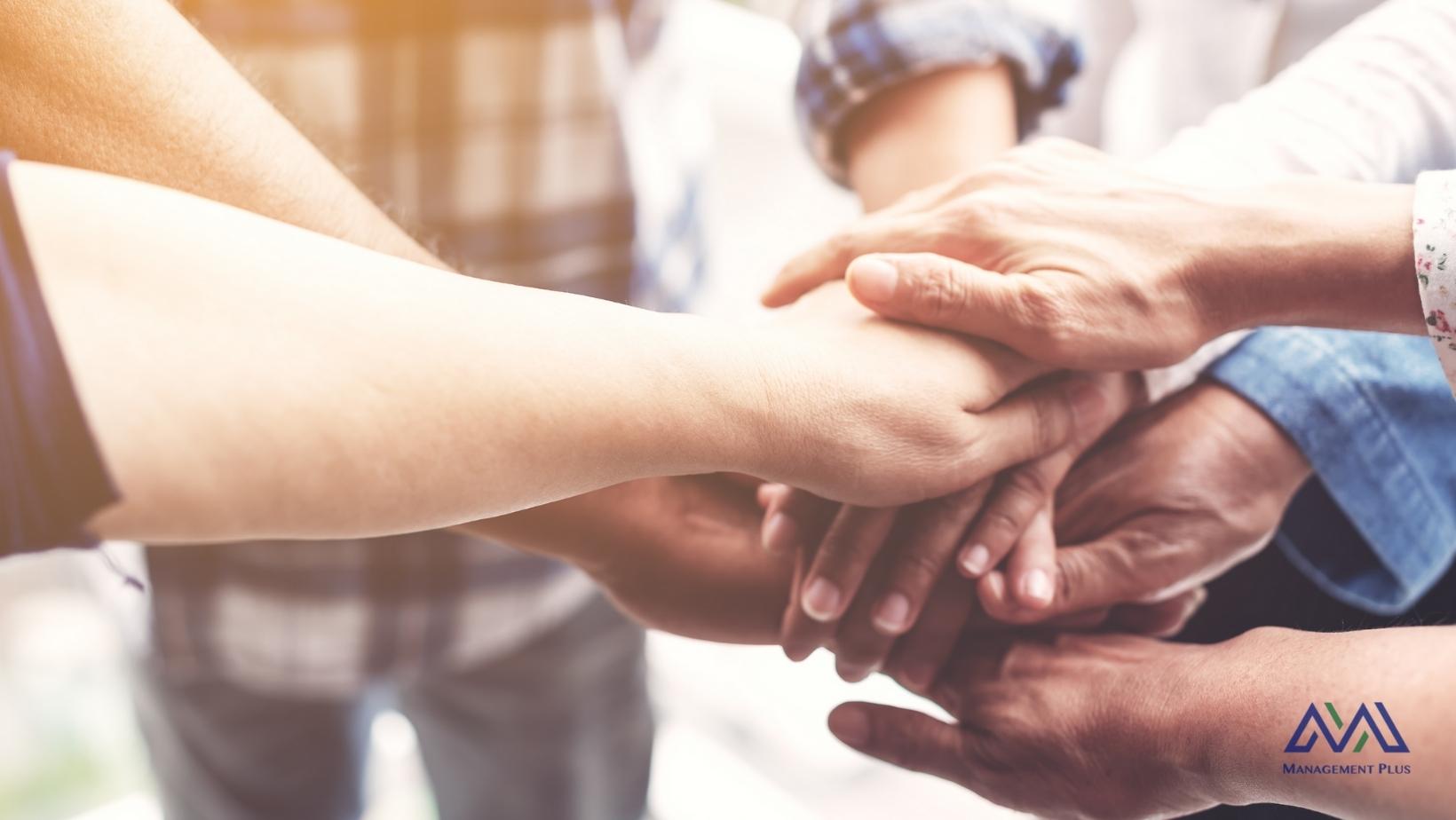 Image contains five hands on top of each other in a gesture of friendship.
